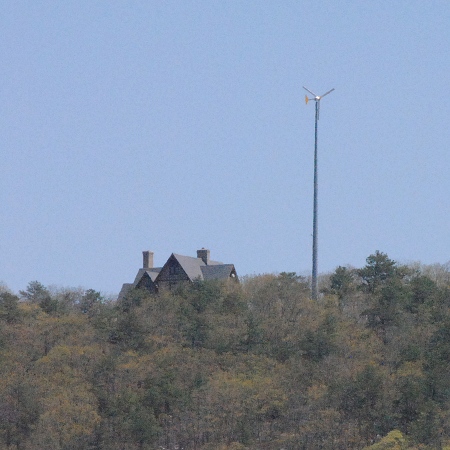 Nice house with windmill on top of the hill next to the fields.